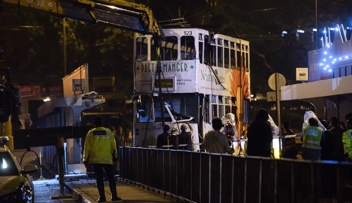 Personel layanan darurat mengamati evakuasi sebuah trem double-decker yang terbalik di jalan utama di Hong Kong, Kamis (6/4). Belum jelas penyebab kecelakaan, namun kemungkinan akibat pengemudi gagal mengendalikan kendaraan tersebut. (ANTHONY WALLACE/AFP)