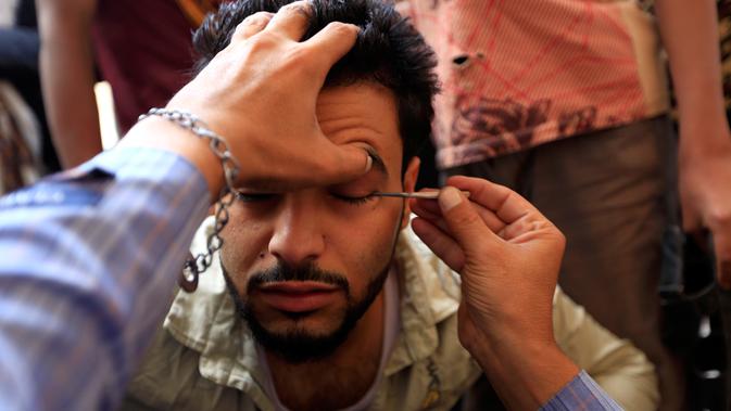 Seorang pria Yaman saat kelopak matanya dirias dengan kosmetik tradisional kohl di Masjid Agung, kota tua Sanaa pada 9 mei 2019. Bagi muslim Yaman, pemakaian kohl diyakini mampu membersihkan dan melindungi mata dari penyakit ini sudah menjadi tradisi setiap bulan Ramadan. (MOHAMMED HUWAIS/AFP)