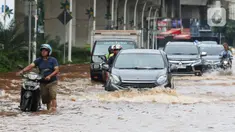 Pengendara terpaksa mendorong motornya saat melintasi genangan air di Jalan Boulevard Raya, Kelapa Gading, Jakarta, Rabu (29/1/2025). (Liputan6.com/Herman Zakharia)