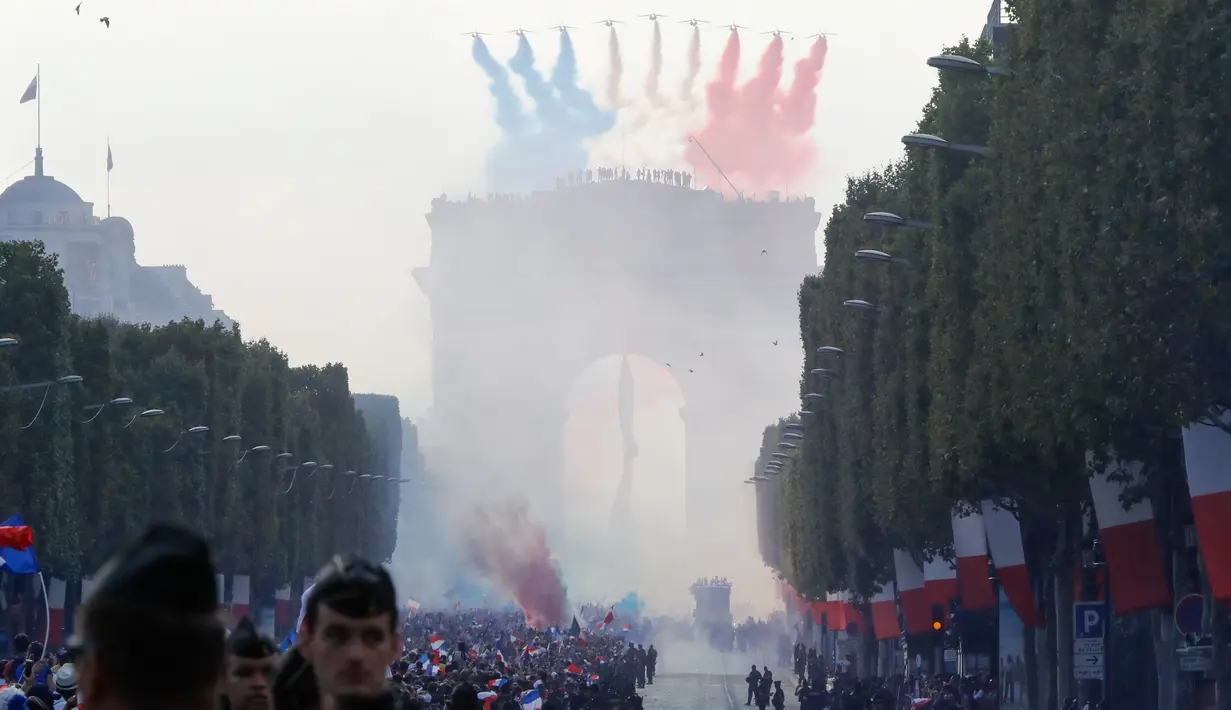 Peswat tempur melepaskan asap berwarna bendera Prancis menyambut kedatangan Les Bleus di Arch of Triumph, Paris, (16/7/2018). Parade tersebut adalah bagian dari perayaan Prancis meraih trofi Piala Dunia 2018. (AFP/Francois Guillot)