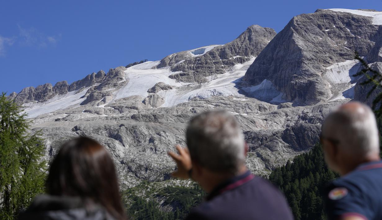Dua petugas Carabinieri menunjukkan kepada seorang jurnalis gletser Punta Rocca sehari setelah bongkahan besar gletser runtuh mengirimkan longsoran es, salju, dan batu ke pejalan kaki di dekat Canazei, di Pegunungan Alpen Italia di Italia utara (4/7/2022).  (AP Photo/Luca Bruno)