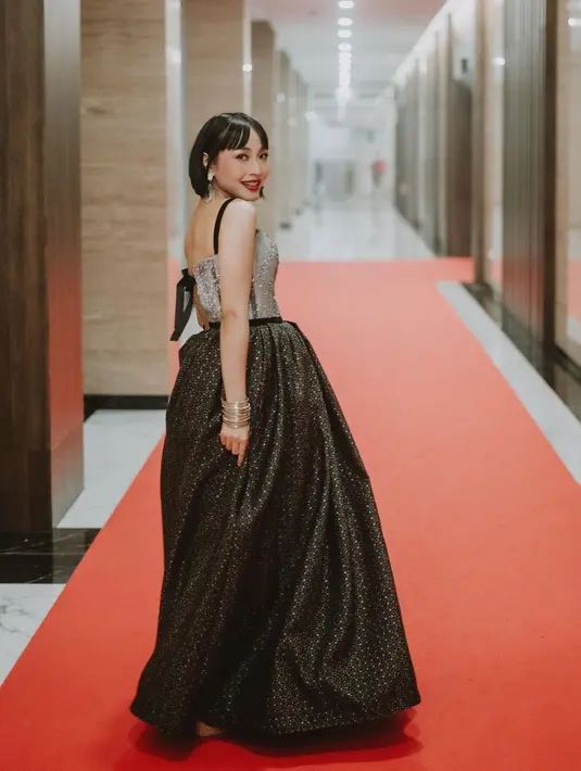 Seperti saat datang di AMI Awards 2022, ia tampil glamor mengenakan gaun hitam dengan aksen payet silver. [Instagram/rinni_w].