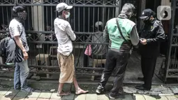 Petugas memeriksa suhu tubuh warga sebelum memasuki area layanan makan gratis di Jalan Basuki Rachmat, Cipinang Muara, Jakarta, Senin (8/3/2021). Sebagian besar yang datang mayoritas berprofesi kuli bangunan, pengamen, petugas taman kota hingga pengemudi ojek online. (merdeka.com/Iqbal S Nugroho)