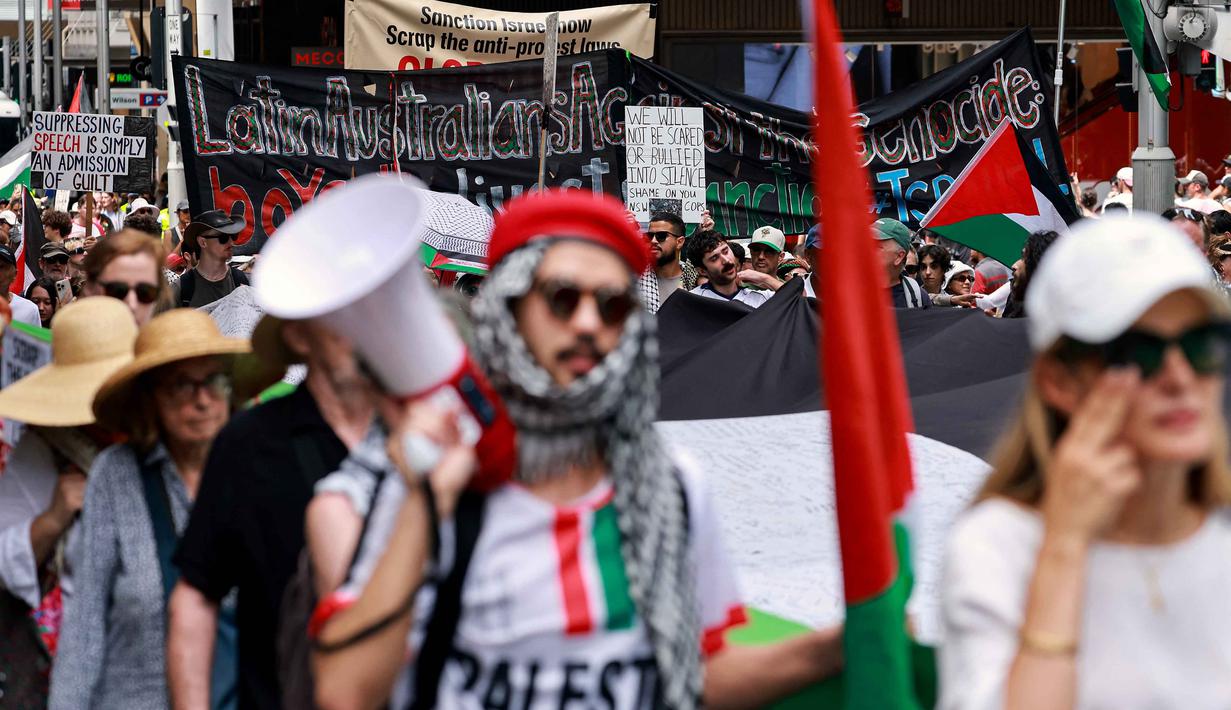 Aksi ini merupakan bagian dari gelombang protes berkelanjutan di Australia yang menuntut keadilan bagi warga Palestina di kota Gaza. Tampak dalam foto, para demonstran pro-Palestina membawa bendera, spanduk, dan plakat saat mereka berbaris berunjuk rasa di jalanan kota Sydney, Australia, Minggu 22 Februari 2026. (DAVID GRAY/AFP)