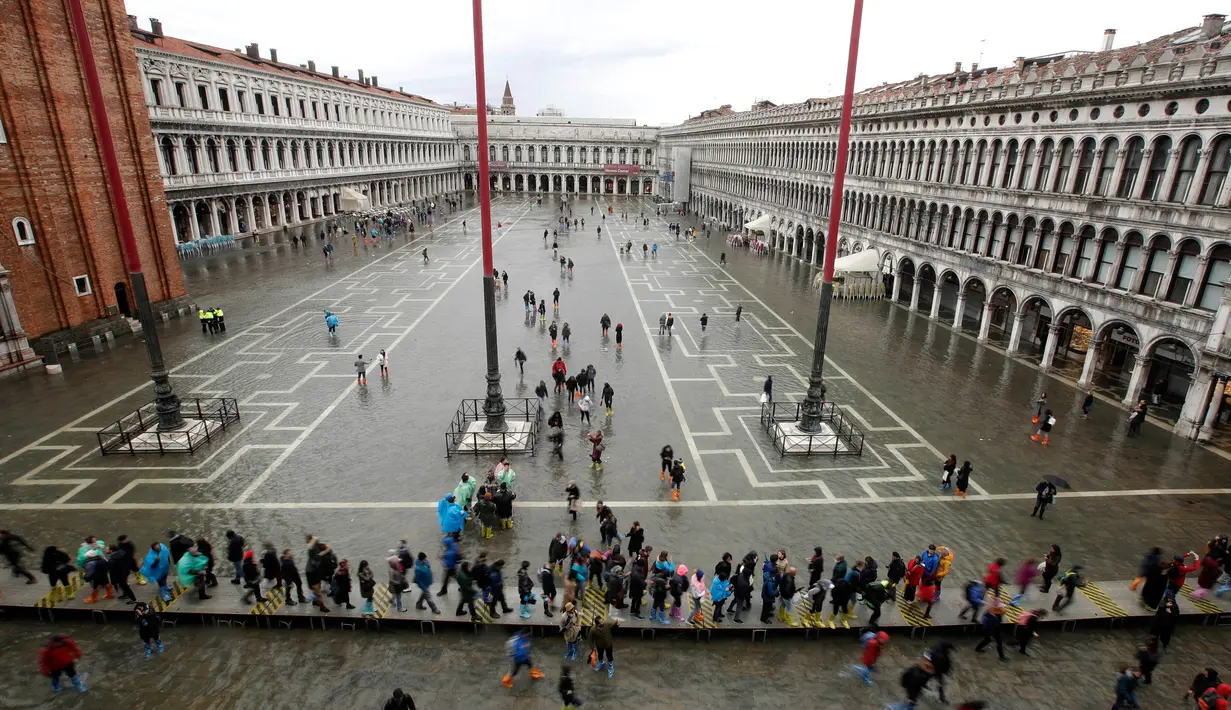 Warga berjalan di Alun-Alun Santo Markus yang banjir akibat terjangan gelombang pasang di Venesia, Italia, Selasa (12/11/2019). Venesia dilanda banjir akibat gelombang pasang setinggi 127 cm. (AP Photo/Luca Bruno)