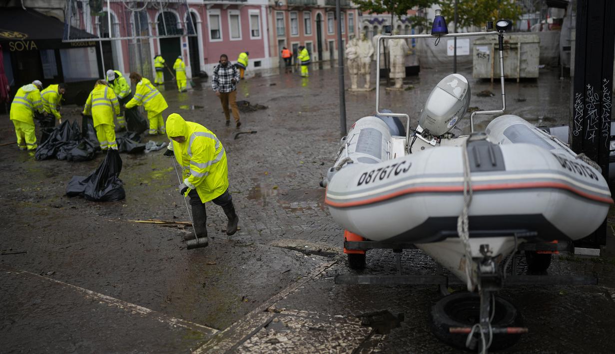 Pekerja kota membersihkan jalan yang terendam banjir semalam di Alges, tepat di luar Lisbon, Selasa (13/12/2022). Badai Atlantik menghantam semenanjung Iberia, meninggalkan jejak kehancuran pada Selasa, terutama di Ibu kota Portugal,  Lisbon, sebelum pindah ke timur ke Spanyol.  (AP Photo/Armando Franca)