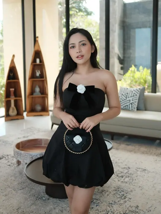 Rachel Vennya tampil manis mengenakan outfit serba hitam. Kali ini ia mengenakan strapless mini dress dengan detail pita dan bentuk bunga mawar putih di bagian tengahnya, menenteng tas mini yang juga berwarna hitam. [Foto: Instagram/rachelvennya]