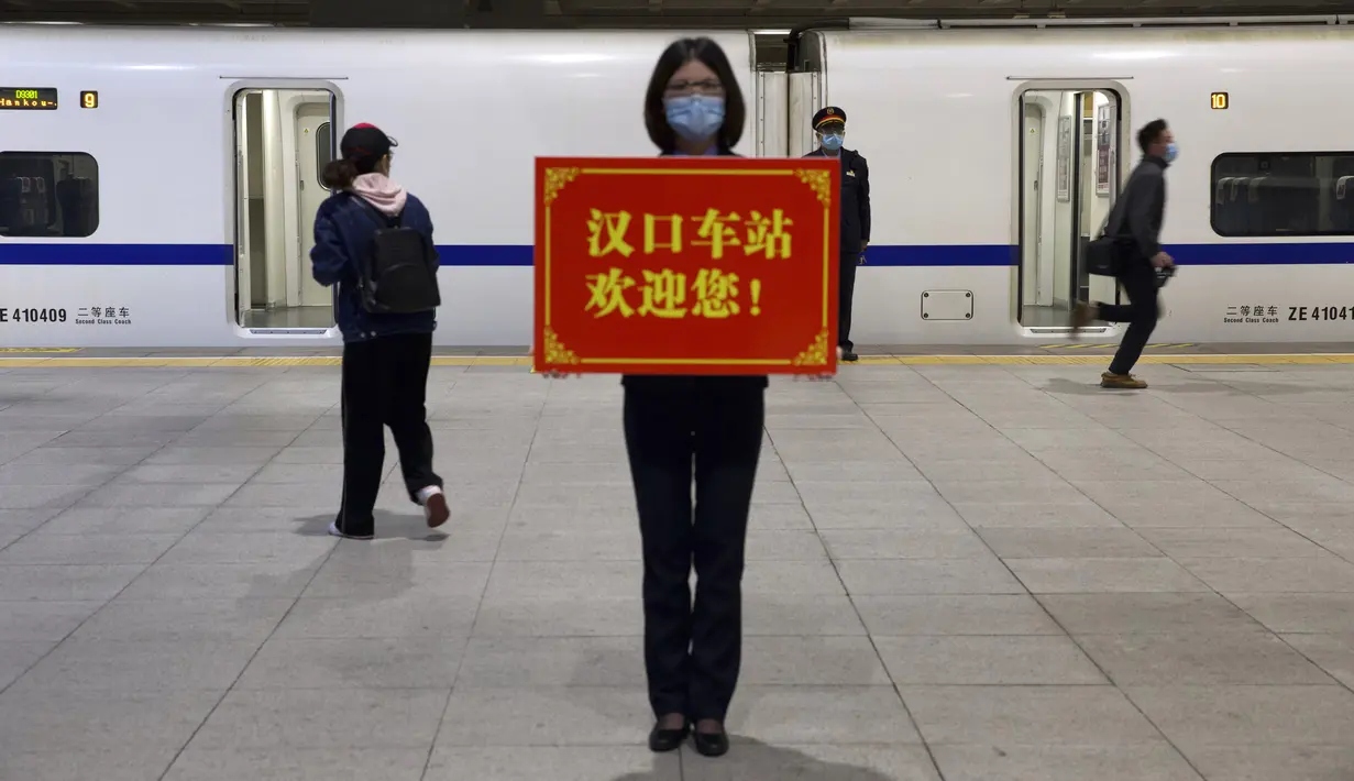 Petugas memegang papan bertuliskan ‘Stasiun Hankou menyambut Anda!’ saat para penumpang menaiki kereta pertama yang beroperasi usai berakhirnya lockdown akibat pandemi virus corona COVID-19 di Stasiun Hankou, Wuhan, Provinsi Hubei, China, Rabu (8/4/2020). (AP Photo/Ng Han Guan)