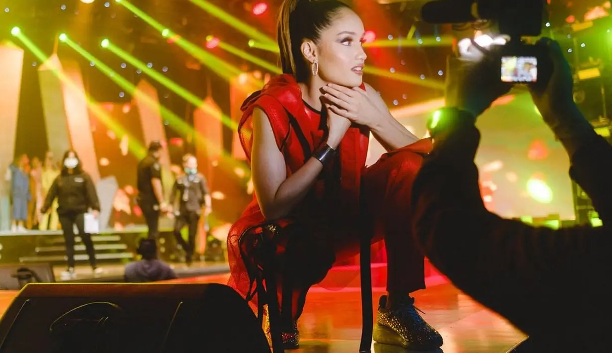 Cinta Laura tampil menawan di atas panggung dengan outfit merah. Detail gaun yang dikenakannya ini memiliki bahu asimetris dan high slit di bagian roknya. [Foto: Instagram/claurakiehl]