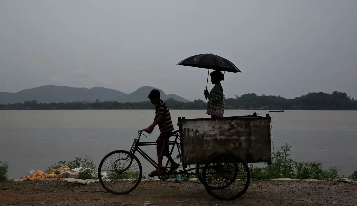 Seorang anak membonceng adiknya menggunakan sepeda gerobak saat hujan mengguyur Gauhati, India, Selasa (30/5). Beberapa negara bagian di India timur laut mengalami hujan deras sebagai efek topan Mora yang melanda selatan Bangladesh. (AP Photo/Anupam Nath)