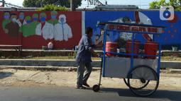 Pedagang lewat depan mural bertemakan COVID-19 di kawasan Manggarai, Bukit Duri, Jakarta, Jumat (28/8/2020). Mural tersebut dibuat untuk meningkatkan kepatuhan masyarakat akan protokol kesehatan karena kasus COVID-19 nasional terus meningkat. (merdeka.com/Imam Buhori)