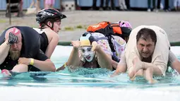 Tiga peserta melintasi kolam sambil menggendong istrinya selama kompetisi Wife Carrying World Championships di Sonkajarvi, Finlandia, 2 Juli 2016. Pemenang kompetisi ini adalah mereka yang tercepat mencapai finish. (Timo Hartikainen/Lehtikuva/AFP)