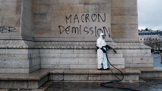 Pekerja membersihkan grafiti bertuliskan 'pengunduran diri Macron' di Arc de Triomphe, Paris, Prancis, Minggu (2/12). Aktivis membakar mobil, menghancurkan jendela, dan menjarah toko saat memprotes kenaikan pajak bahan bakar. (AP Photo/Thibault Camus)