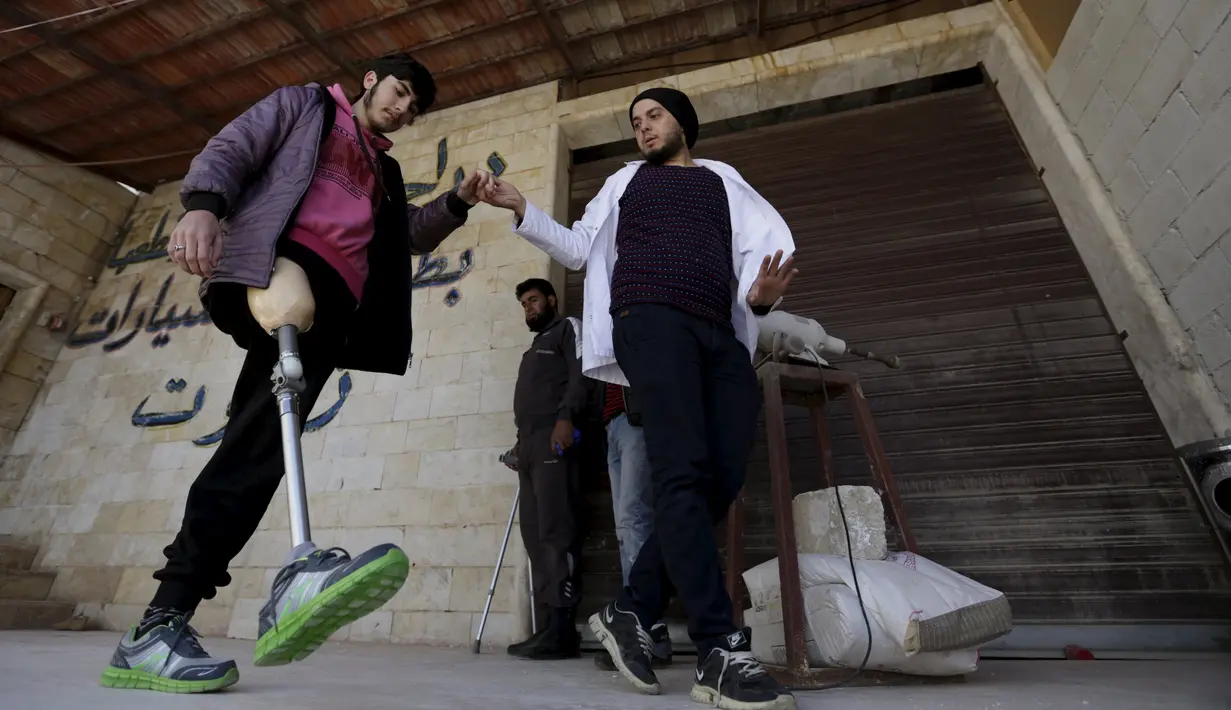 Seorang pekerja pembuat anggota badan buatan, Khamis (kanan) membantu seorang pria berjalan menggunakan kaki palsu di kota Maaret al - Numan di provinsi Idlib , Suriah 20 Maret 2016. (REUTERS / Khalil Ashawi)