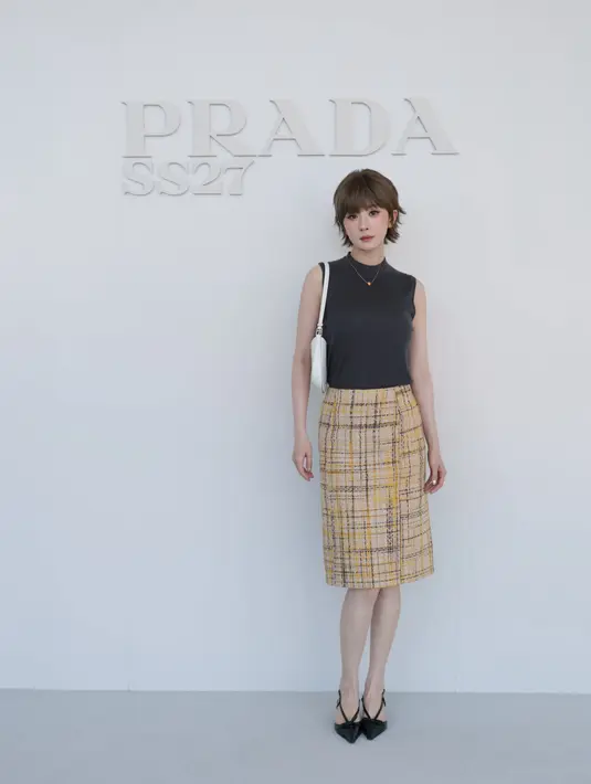 Yang Mi kenakan atasan tanpa lengan abu-abu gelap, dipadukan rok pensil bermotif plaid kuning-hitam, tas selempang putih, dan heels slingback hitam [dok. Prada]
