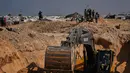 Warga Palestina menyaksikan aktivitas pekerja Mesir yang menggunakan alat berat untuk mencari jenazah para sandera di Kota Hamad, Khan Younis, di Jalur Gaza selatan, Selasa 28 Oktober 2025. Di Khan Younis, proses penggalian tanah terlihat menggunakan alat berat di tengah reruntuhan. (AP Photo/Abdel Kareem Hana)