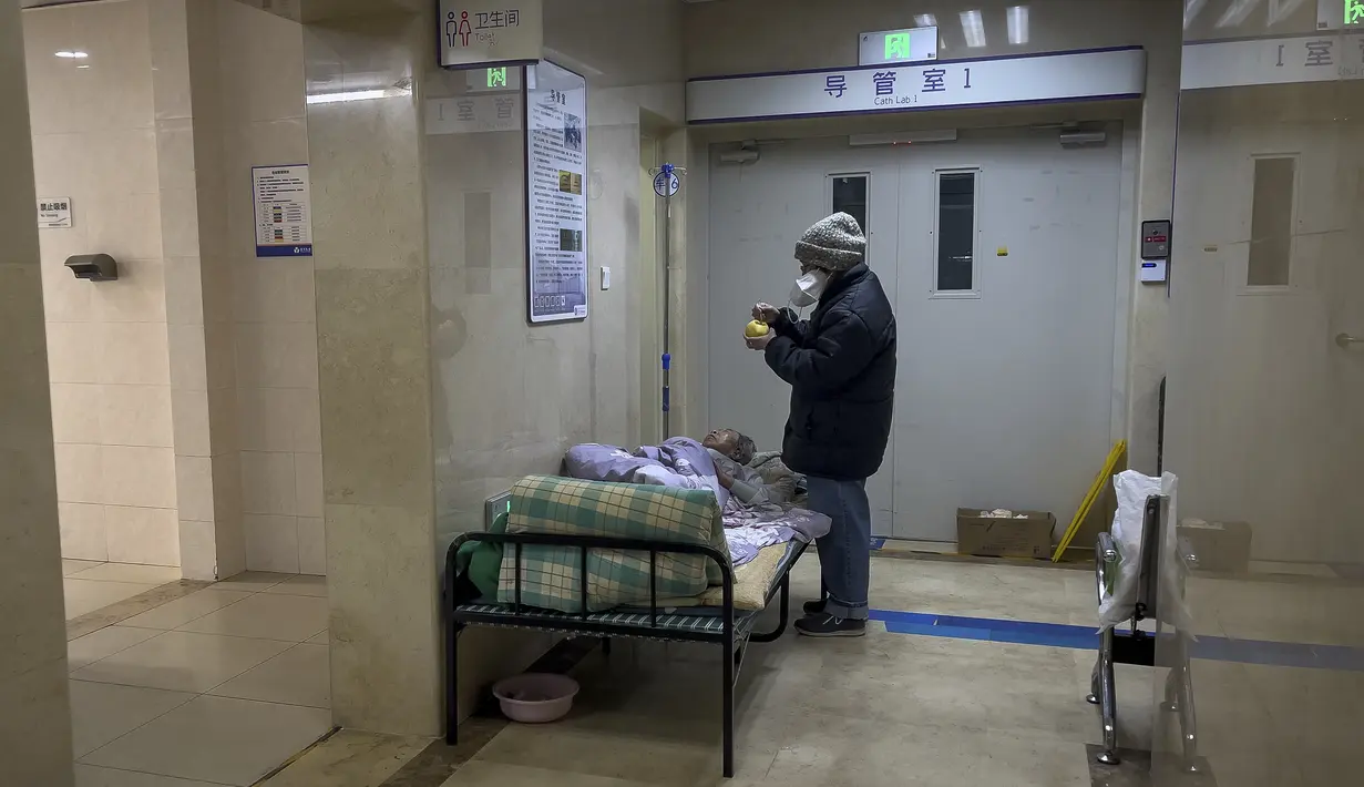 Seorang perempuan merawat kerabatnya yang sudah lanjut usia di koridor bangsal darurat untuk menerima infus di sebuah rumah sakit di Beijing, Kamis (5/1/2023). Pasien, kebanyakan dari mereka lansia, berbaring di tandu di lorong dan menerima oksigen sambil duduk di kursi roda saat kasus COVID-19 melonjak di ibu kota China, Beijing. (AP Photo/Andy Wong)