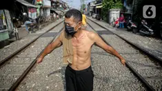 Seorang pria berjemur di bantaran rel di kawasan pemukiman padat Pejompongan, Jakarta, Selasa (6/7/2021). Berjemur diri di bawah matahari di antara pukul 08.00-11.00 WIB merupakan salah satu upaya yang paling sederhana untuk menjaga kesehatan selama wabah virus COVID-19. (Liputan6.com/Faizal Fanani)