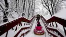 Seorang pria menarik putrinya menaiki tangga di dekat museum Kolomenskoye di Moskow (4/2). Namun, meskipun banyak kekacauan, banyak warga yang senang dengan salju yang menyelimuti Moskow. (AFP/Yuri Kadobnov)