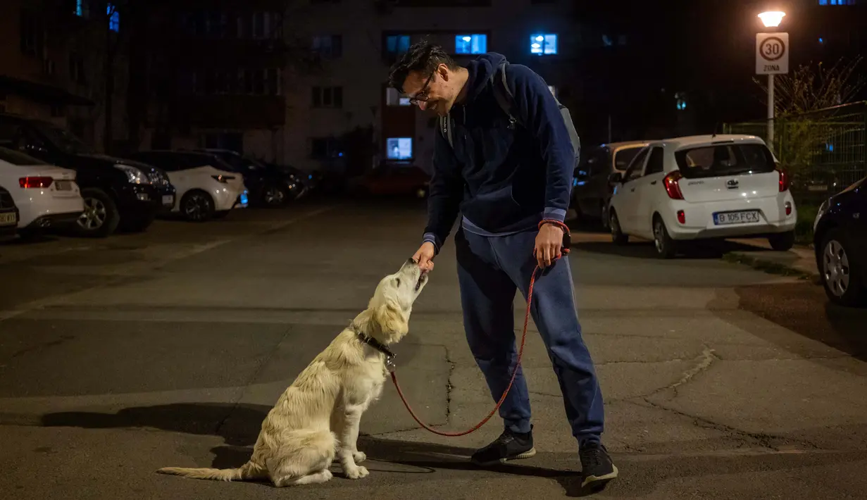Iulian Barbulescu (34) berpose dengan anjingnya Jesse  (5 bulan) di Bucharest (28/3/2020). Undang-undang militer, yang disahkan pemerintah Rumania untuk mengurangi penyebaran virus corona, menyatakan berjalan bersama anjing adalah salah satu  kegiatan yang masih diizinkan. (AFP/Andrei Pungovschi)