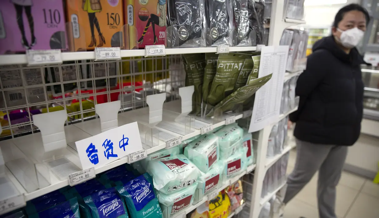 Seorang wanita berjalan melewati rak-rak masker wajah dengan tanda yang bertuliskan "restocking" di sebuah toko di Beijing (28/1/2020). Virus ini pertama kali ditemukan di Wuhan, China. Kemudian menyebar dan menyebabkan kematian mencapai 160 orang. (AP Photo/Mark Schiefelbein)