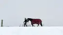 Seorang gadis muda berjalan dengan kudanya saat salju tebal turun di dekat desa kecil Pistheim, Munich, Jerman, Selasa (27/2). (CHRISTOF STACHE/AFP)