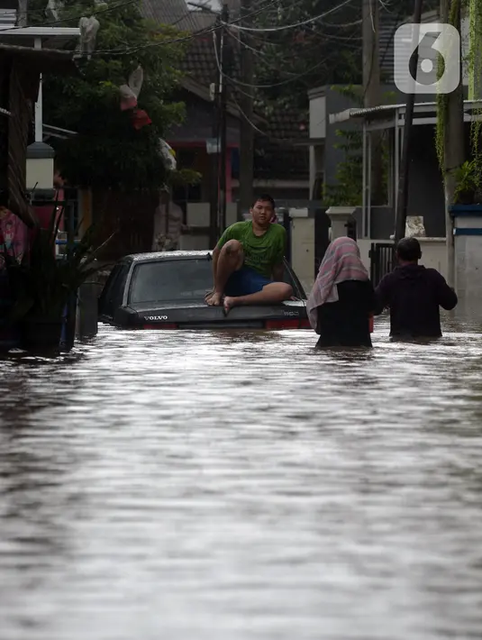 Warga duduk di atas mobil saat banjir merendam jalan dan rumah di RT 003/05, Pejaten, Jakarta, Sabtu ( 20/2/2021). Curah hujan yang tinggi sejak malam hingga dini hari mengakibatkan sejumlah kawasan terendam banjir. (merdeka.com/Imam Buhori)