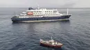 Pemandangan udara sebuah kapal ambulans yang membawa awak yang mengenakan pakaian pelindung bahan berbahaya (hazmat suit) saat mereka mendekati pintu kemudi di sisi kanan kapal pesiar MV Hondius, ketika kapal tersebut berhenti di lepas pelabuhan Praia, ibu kota Tanjung Verde, Selasa 5 Mei 2026. Kapal pesiar MV Hondius saat ini masih tertahan di lepas pantai Praia, Tanjung Verde. (Foto oleh AFP)