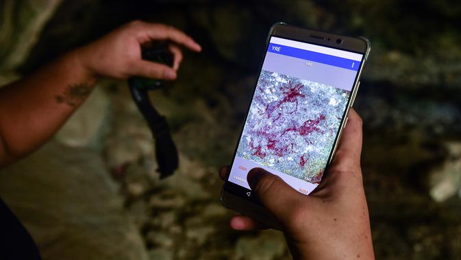 Seorang arkeolog dari Departemen Seni Rupa di Ratchaburi menggunakan aplikasi di ponsel untuk melihat lukisan gua yang baru ditemukan di taman nasional Khao Sam Roi Yot di pesisir provinsi Prachuap Kiri Khan (10/9/2020). (AFP/Lillian Suwanrumpha)
