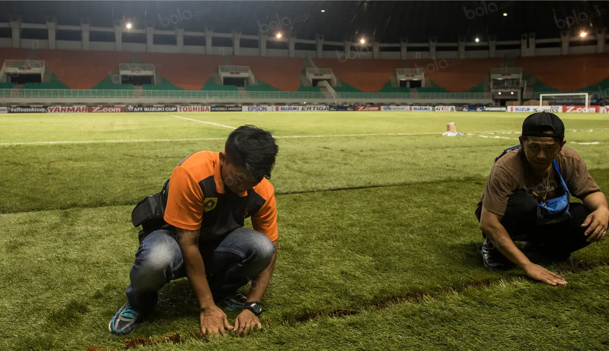Pekerja merapihkan rumbut sintetis saat persiapan jelang laga semifinal Piala AFF 2016 antara Timnas Indonesia melawan Vietnam di Stadion Pakansari, Jawa Barat, Jumat (3/12/2016). (Bola.com/Vitalis Yogi Trisna)