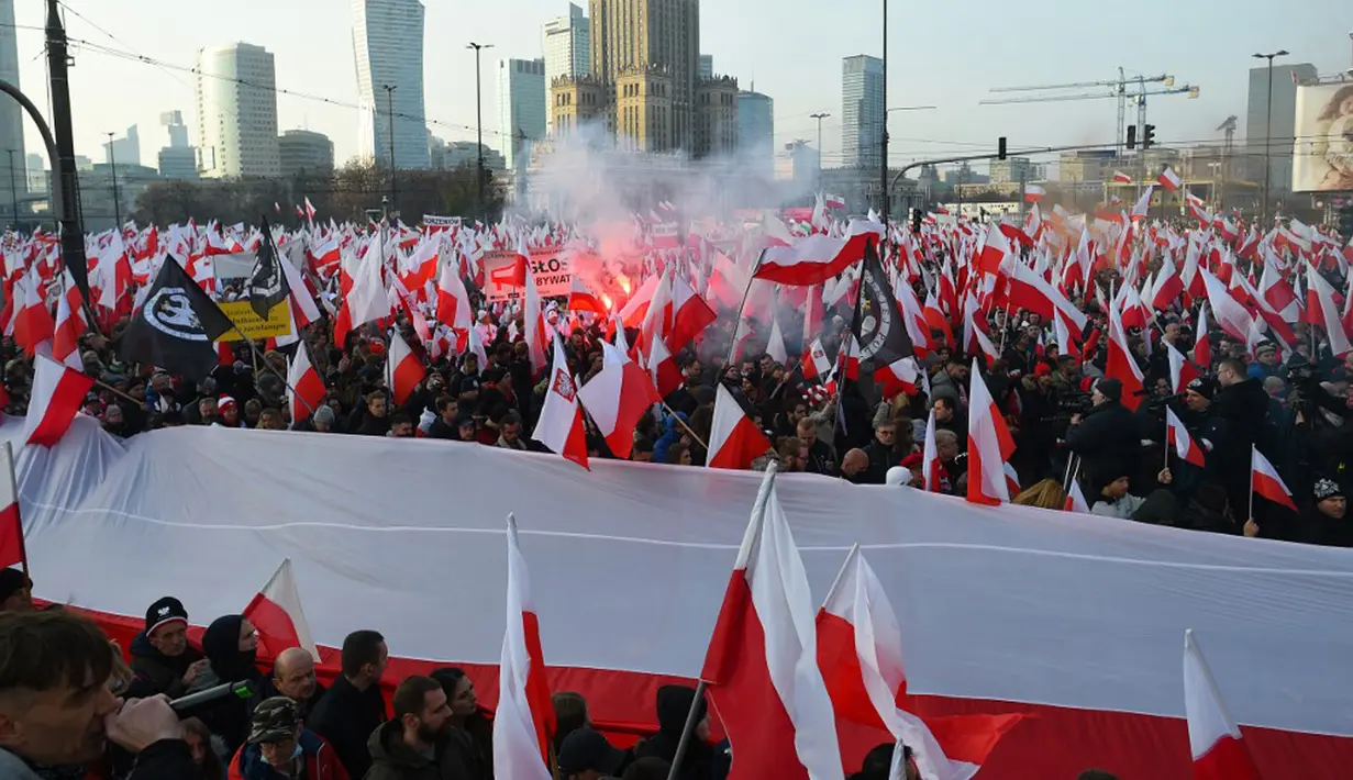 Orang-orang mengibarkan bendera nasional Polandia saat pawai untuk menandai Hari Kemerdekaan Nasional Polandia di Warsawa, Polandia, 11 November 2021. Hari Kemerdekaan Nasional Polandia dirayakan pada 11 November untuk memperingati ulang tahun Republik Polandia Kedua. (Adam Chelstowski/AFP)