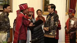 Pemangku Hutan Adat dari Tombak Haminjon (Kemenyan) Provinsi Sumatera Utara saat memberikan kain ulos kepada Presiden Joko Widodo (Jokowi) usai pencanangan pengakuan Hutan Adat di Istana Negara, Jakarta, Jumat (30/12). (Liputan6.com/Faizal Fanani)