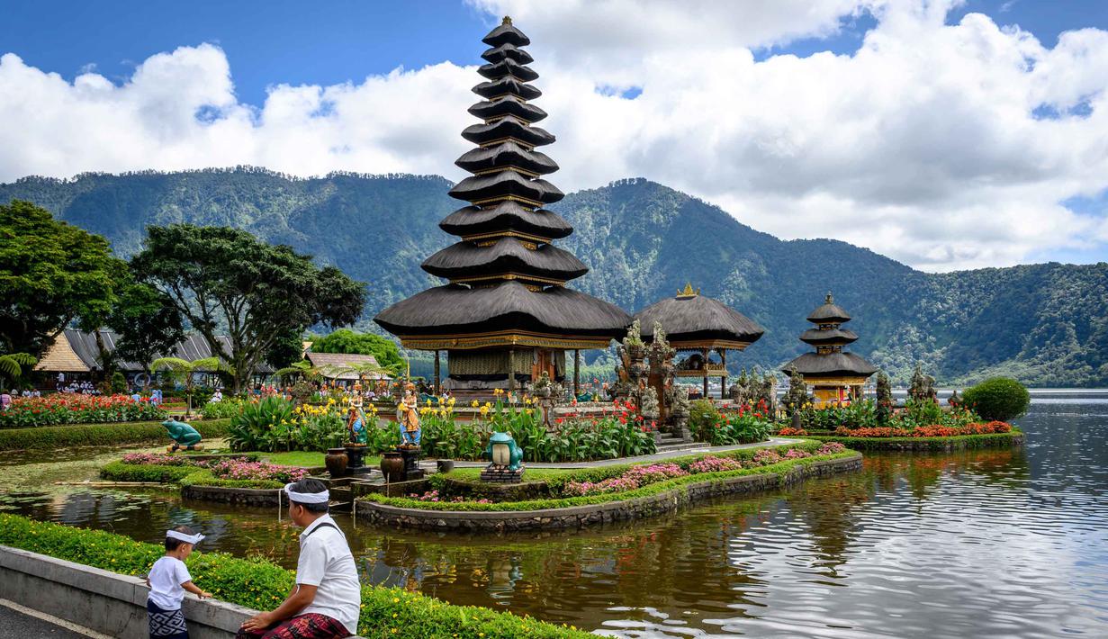Berlatar belakang perbukitan serta pegunungan yang hijau menambah nilai estetika panorama pura ini. Tampak dalam foto, seorang pria duduk di depan Pura Ulun Danu Beratan, sebuah pura Hindu di Danau Beratan dekat Bedugul, Bali, pada Jumat 7 November 2025. (Mladen ANTONOV/AFP)