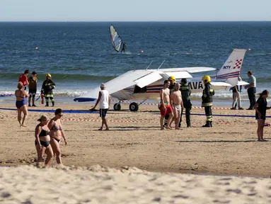Sejumlah orang berjalan melewati sebuah pesawat kecil yang melakukan pendaratan darurat di pantai Sao Joao yang ramai dekat Lisbon, Portugal, Rabu (2/8). Akibatnya, pesawat itu melindas dua pengunjung pantai yang sedang berjemur. (AP Photo/Armando Franca)