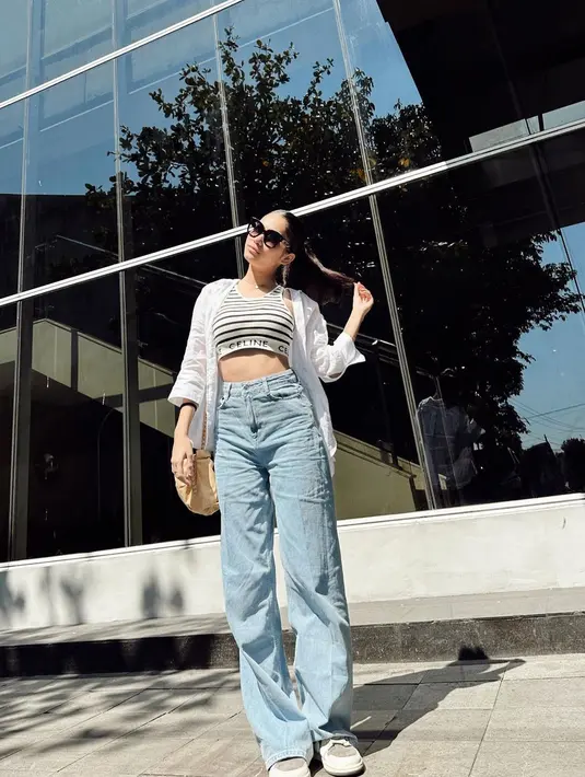 Gaya kasual yang minimalis namun menawan ala Azizah Salsha. Ia memadukan cropped top bermotif garis, ditumpuknya dengan kemeja putih dengan kancing dibuka, dan celana jeans panjang. [Foto: Instagram/azizahsalsha_]