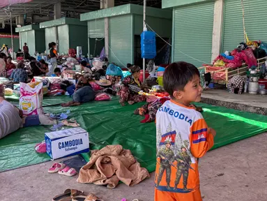 Seorang anak laki-laki mengenakan kaus bergambar tentara berjalan melewati pengungsi lain yang beristirahat di kamp sementara di provinsi Banteay Meanchey pada Sabtu 13 Desember 2025, di tengah bentrokan di sepanjang perbatasan Kamboja-Thailand. Ketegangan di perbatasan Kamboja-Thailand kembali mencapai titik kritis. (Suy Se/AFP)
