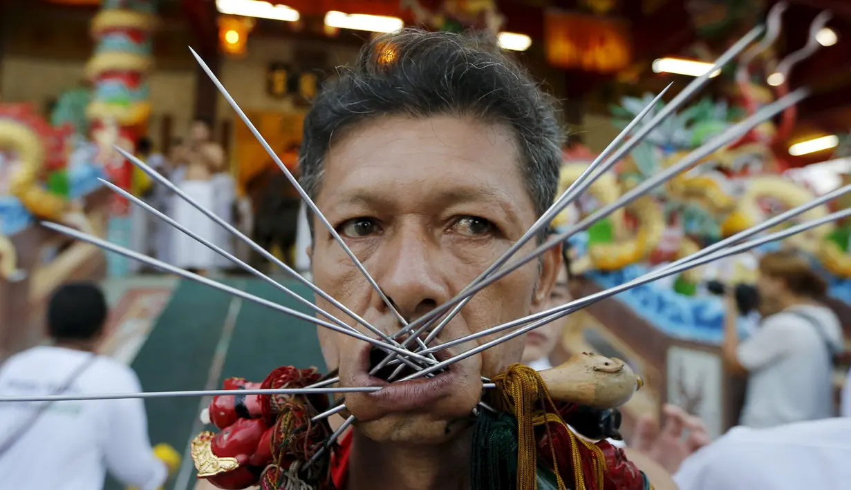 Seorang pemuja dari Kuil Samkong menusukkan benda tajam ke pipi saat memeriahkan festival vegetarian di Phuket, Thailand (17/10/2015). Festival ini menampilkan aksi ekstrem pemuja dengan menusukkan benda tajam ke wajah. (REUTERS/Jorge Silva)