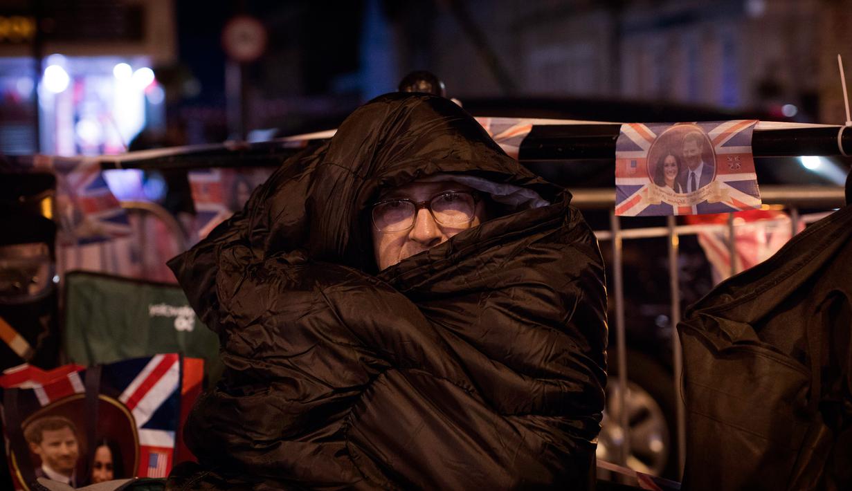 Seorang penggemar beristirahat di trotoar pinggir jalan di luar Kastil Windsor, Inggris (16/5). Para penggemar ingin menyambut langsung iring-iringan kendaraan yang mengarak Pangeran Harry dan pasangannya Meghan Markle. (AP Photo / Emilio Morenatti)