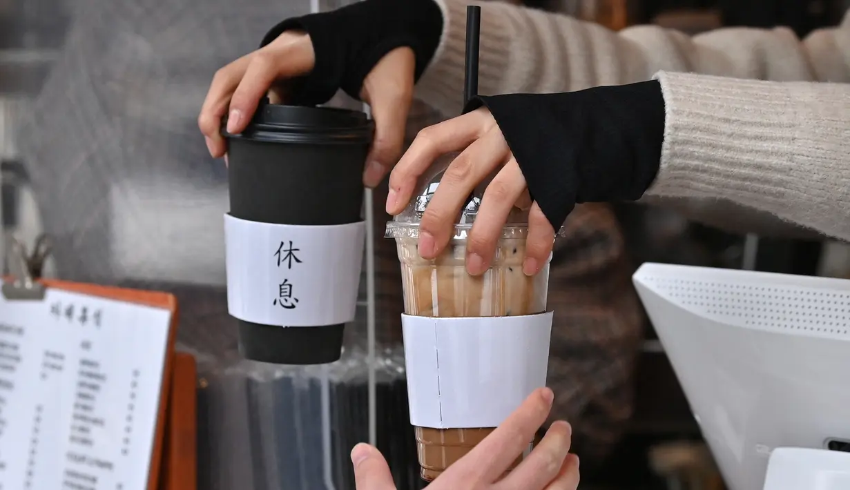 Gambar pada 26 Januari 2023 ini memperlihatkan seorang karyawan membagikan minuman kopi panas dan dingin kepada seorang pelanggan di sebuah kafe di Seoul, Korea Selatan. Budaya kopi bahkan telah melahirkan bahasanya sendiri. Iced Americano dikenal sebagai "Ah-Ah" dan peminum beratnya dikenal sebagai "Eoljuka", kontraksi dari peribahasa baru yang menyatakan  mereka akan mati kedinginan untuk minuman mereka.  (Jung Yeon-je / AFP)