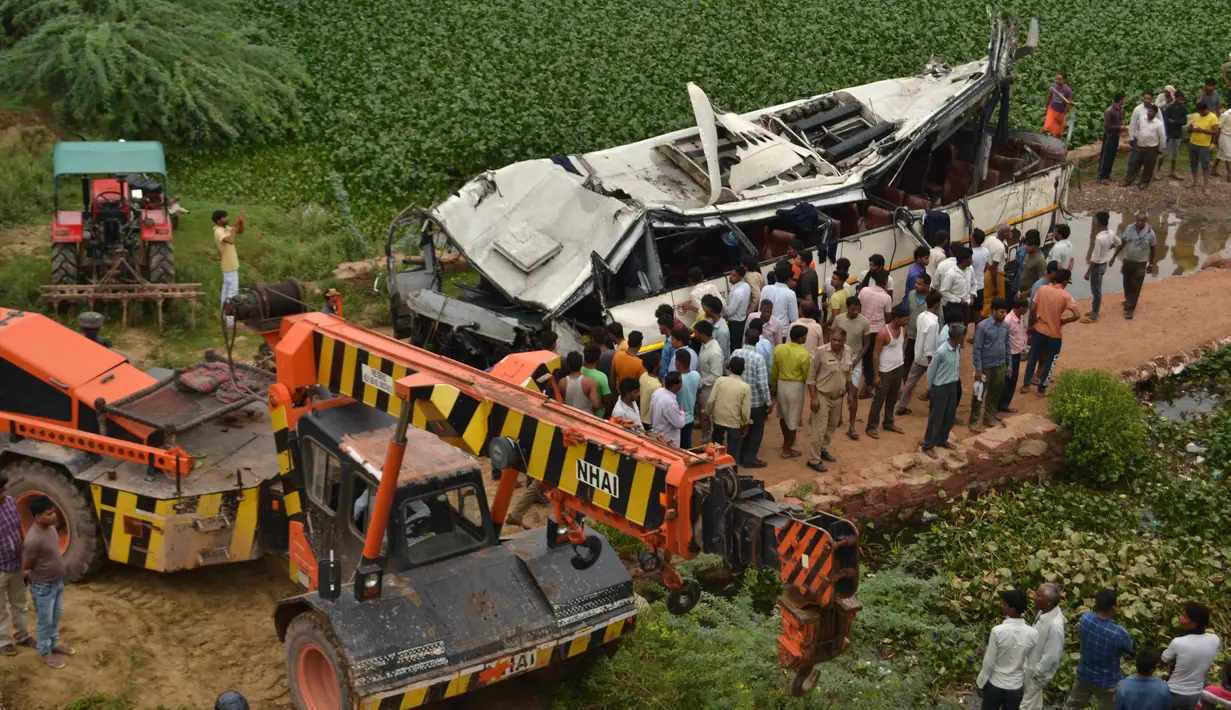 Warga dan polisi menyaksikan bus tingkat yang rusak usai mengalami kecelakaan di jalan bebas hambatan di Agra, India, Senin (8/7/2019). Kecelakaan terjadi sekitar pukul 04.15 waktu setempat saat bus melakukan perjalanan dari Lucknow menuju New Delhi. (Pawan Sharma/AFP)