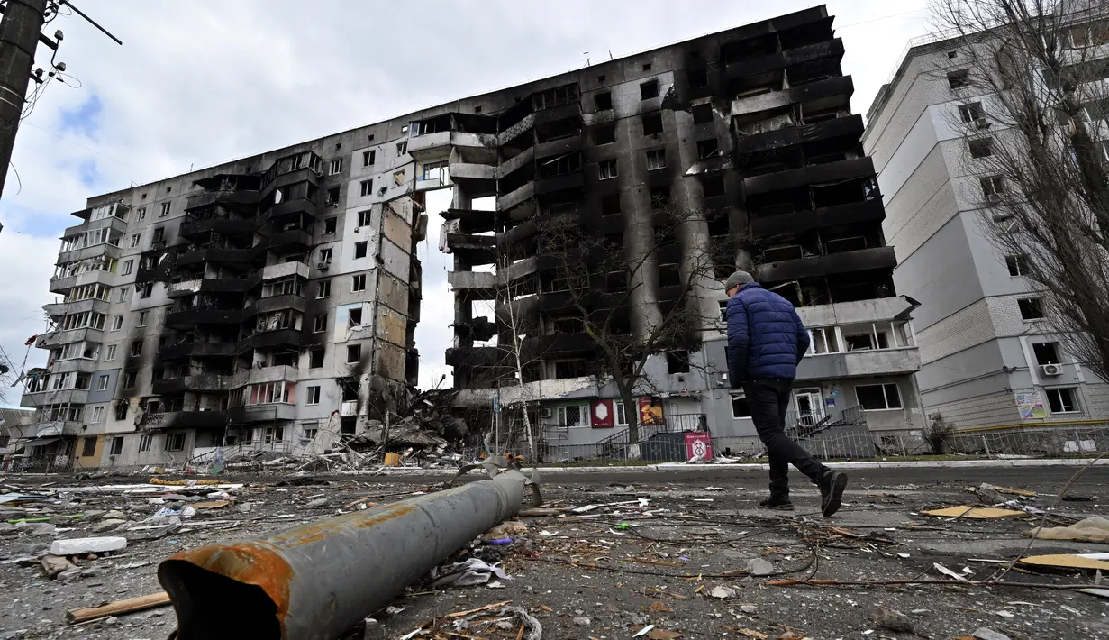 Seorang pria berjalan melewati pecahan persenjataan yang berserakan di jalan saat melewati bangunan yang hancur di kota Borodianka, barat laut Kiev pada 4 April 2022. Saat pasukan Rusia mundur, kota kecil Borodianka, 50 km barat laut Kiev, menjadi reruntuhan. (Sergei SUPINSKY / AFP)