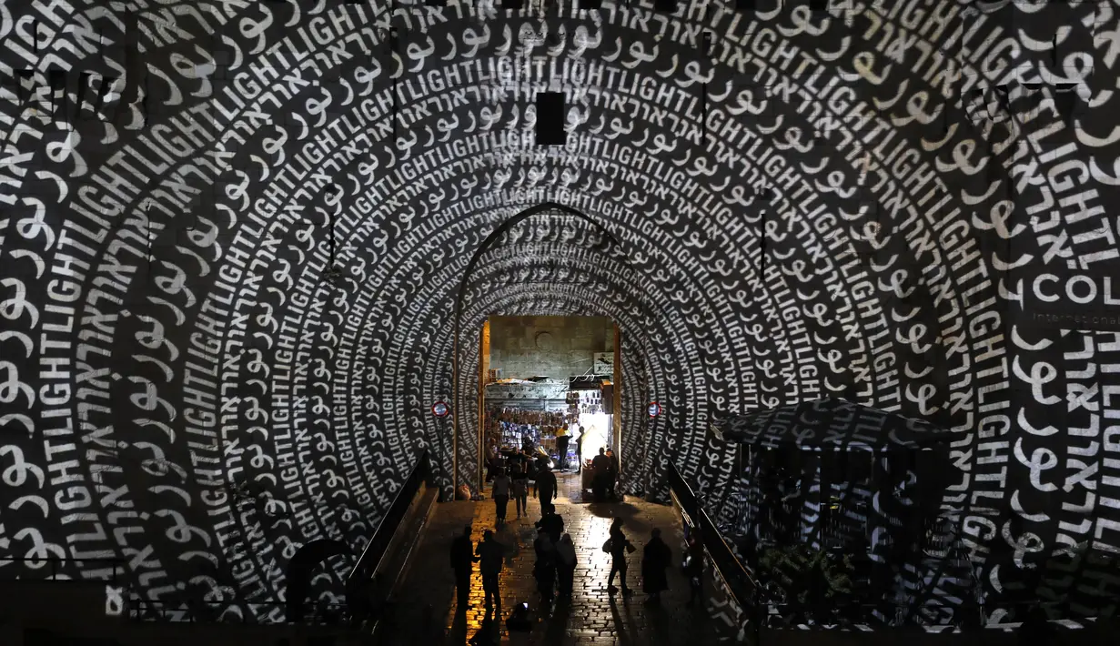 Orang-orang berjalan di dekat gerbang Damaskus selama festival cahaya di kota tua Yerusalem, 28 Juni 2018. Festival cahaya yang menampilkan karya seniman Israel dan internasional ini berlangsung setiap tahun di Kota Tua Yerusalem. (AFP / Ahmad GHARABLI)