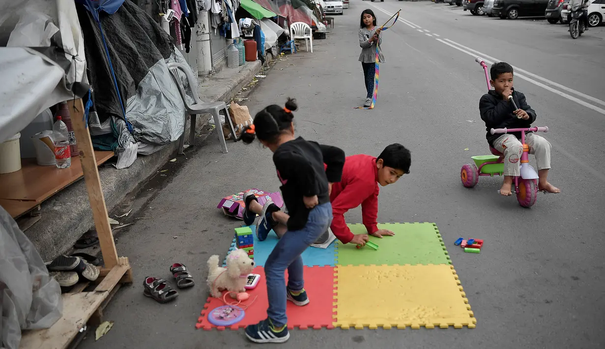 Anak-anak bermain di dekat tenda keluarga mereka yang didirikan di sebuah jalan di luar kamp pengungsi Eleonas di Athena (20/11/2019). Sekitar 14 pengungsi Afghanistan, termasuk keluarga dengan anak-anak, tinggal di luar kamp dalam tenda, tanpa fasilitas apa pun. (AFP/Louisa Gouliamaki)