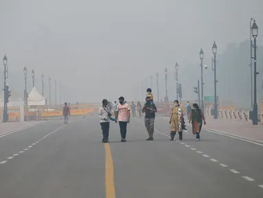 Pejalan kaki berjalan di sepanjang jalan dekat Gerbang India atau India Gate di tengah kabut asap tebal di New Delhi, Kamis (3/11/2022). Kabut asap di New Delhi mencapai tingkat hazardous (berbahaya) pada Kamis 3 November 2022. (Photo by Money SHARMA / AFP)