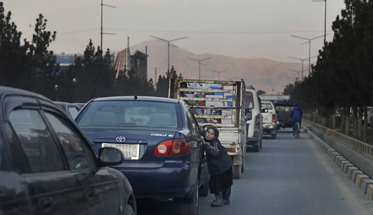 Seorang gadis menempel di pintu mobil sambil meminta sedekah di Kabul, Afghanistan (27/11/2019). Puluhan ribu warga Afghanistan yang terlantar secara internal tinggal di kamp-kamp, yang kekurangan fasilitas dasar, di seluruh Afghanistan. (AP Photo/Altaf Qadri)