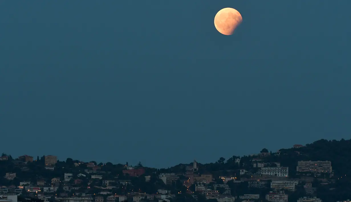 Gerhana bulan parsial terlihat kota Nice, selatan Prancis, Senin (7/8). Gerhana bulan parsial terjadi ketika bumi bergerak di antara bulan dan matahari, tapi tidak persis dalam satu garis. (YANN COATSALIOU / AFP)