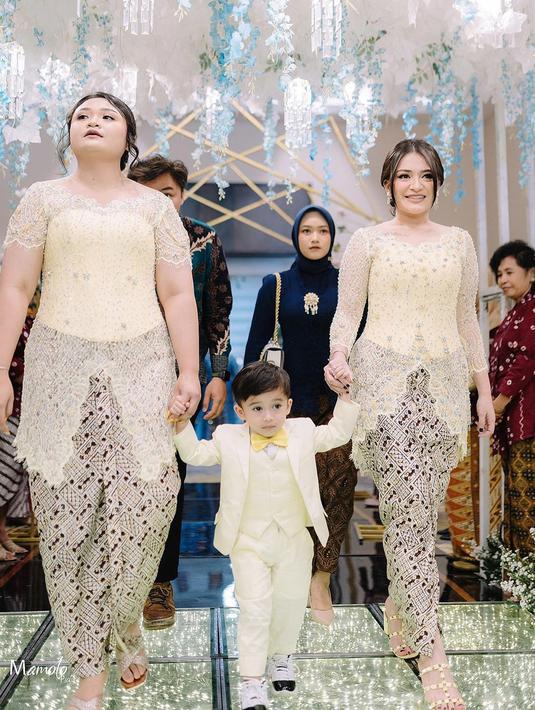 Mantan istri komedian Sule ini menggandeng Adzam yang tampil menggemaskan dengan setelan jas kuning. Warna kuning lembut yang dipilih Nathalie memberikan kesan ceria namun tetap berkelas, seolah menggambarkan suasana bahagia dalam acara pernikahan tersebut. Sepatu hak tinggi berwarna nude juga menyempurnakan gaya keseluruhannya. (Liputan6.com/IG/@nadyaholscher)