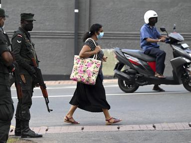 Seorang pejalan kaki melewati tentara yang berjaga di sepanjang jalan di Kolombo pada Sabtu (2/4/2022). Pasukan yang dipersenjatai dengan senapan serbu otomatis dikerahkan di Sri Lanka untuk mengendalikan massa, beberapa jam setelah presiden menyatakan keadaan darurat. (KODIKARA / AFP)