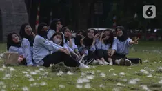 Mahasiswa berfoto di rumput yang bercampur dengan kapas di halaman Institut Pertanian Bogor, Kota Bogor, Jawa Barat, Kamis (25/8/2022). Kapas yang berasal dari pohon kapuk randu yang sedang berguguran itu menjadi daya tarik bagi warga untuk berswafoto. (Liputan6.com/Angga Yuniar)