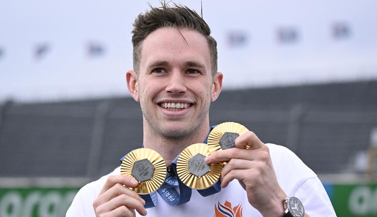 Atlet balap sepeda track Belanda, Harrie Lavreysen memamerkan tiga medali emas Olimpiade Paris 2024 saat bersepeda bareng pembalap Ferrari, Charles Leclerc menjelang Formula 1 GP Belanda di Sirkuit Zandvoort, Kamis (22/08/2024) waktu setempat. (AFP/John Thys)